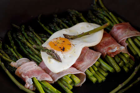 Bacon wrapped asparagus with a fried egg on the topの写真素材