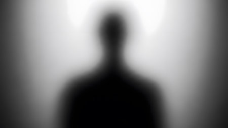 A blurry black silhouette of a person standing against a white background, creating a mysterious and anonymous figure.の素材
