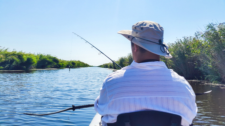 Man standing in an inflatable kayak with a fishing rod, fishing in a water channel with artificial luresの写真素材