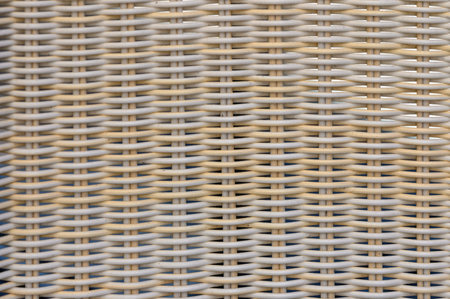 Patterns of a portion of a white wicker chair in front of a blue background