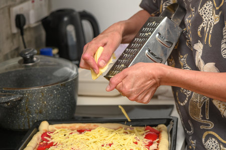 woman prepares pizza with cheese, tomatoes and chicken ham, woman rubs cheese 8の写真素材