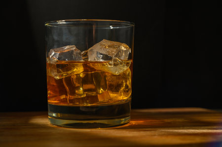 Glass of whiskey on ice with bottle on wood barの写真素材