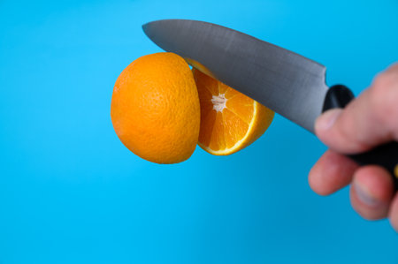knife cutting orange in air on blue backgroundの写真素材