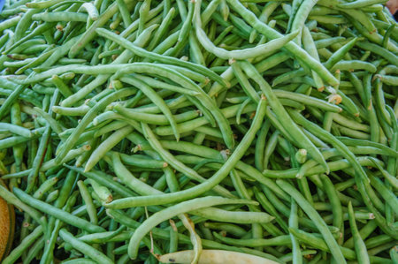 A close-up image of green beans, freshly picked and ready for sale. The beans are stacked in a large...