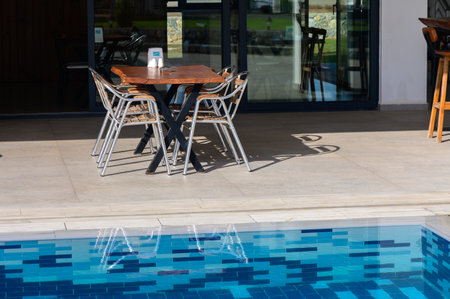 Sunlight dances on the water\'s surface as a table ready stands for guests near the sparkling pool,...