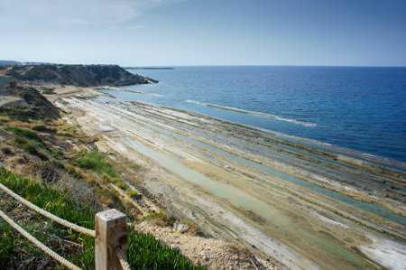 A tranquil expanse along the coastline showcases layered rock formations beneath the calm sea,...