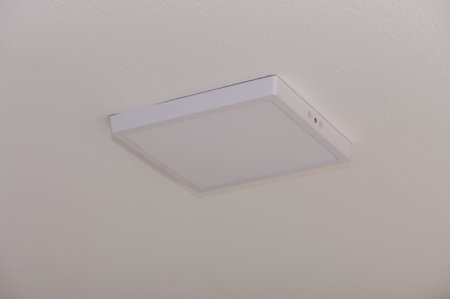A sleek square ceiling light casts a warm glow in the living room, enhancing the cozy atmosphere of...