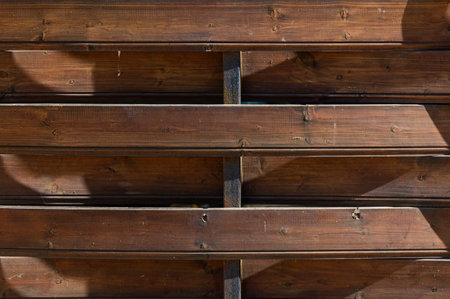 The interplay of light and shadow forms a captivating design on the weathered wooden slats under the...