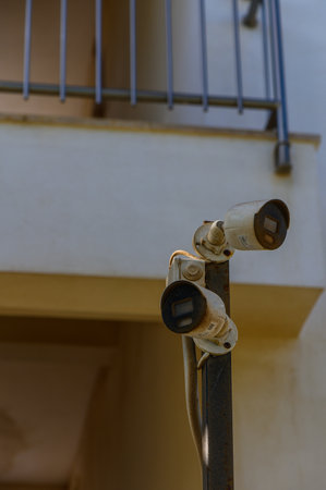 Two surveillance cameras monitor a serene balcony area bathed in warm sunlight.
