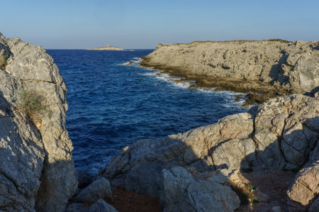 Waves crash against rugged cliffs, creating a serene atmosphere as the sun begins to set along the coast.の写真素材