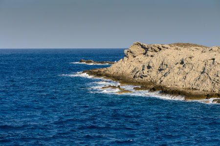 Waves gently lap against rugged cliffs while the sun shines brightly on a serene ocean landscape.