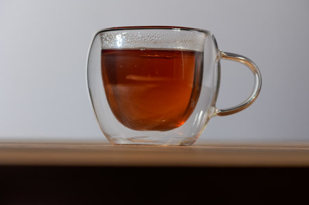 A clear glass cup filled with aromatic tea sits on a wooden surface, reflecting the tranquil atmosphere of the moment.の写真素材