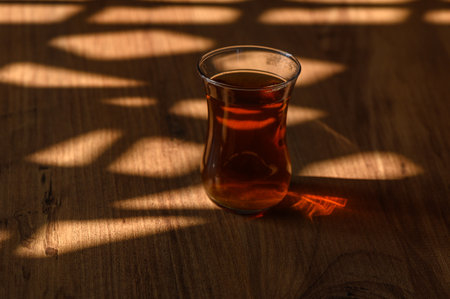 A delicate glass of tea rests on a rustic wooden table, beautifully illuminated by soft afternoon sunlight.の写真素材