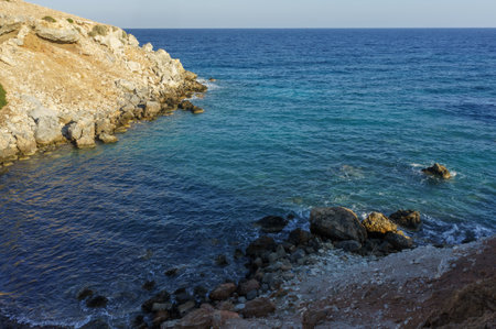 Relax by the calm sea as waves gently lap against the rocky shoreline under a fading sunset.の写真素材