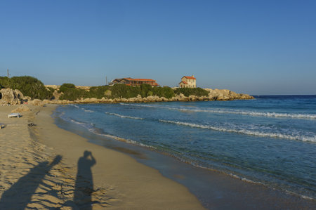 Warm sunlight illuminates a quiet beach as waves gently lap at the shore, creating a peaceful atmosphere.の写真素材