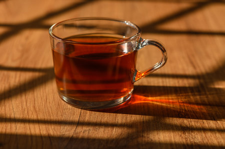 Steam rises from the tea, casting enchanting shadows on the rustic wooden table as afternoon light filters through.の写真素材