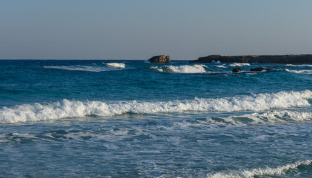 Gentle waves crash softly on the sandy beach as the sun sets, illuminating the tranquil coastal...