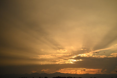 Golden rays of sunlight break through clouds, illuminating a serene landscape as day transitions to...