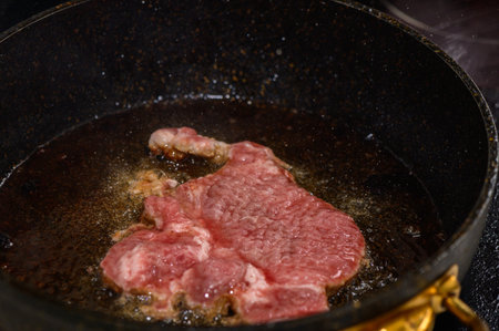 A succulent steak sizzles in hot oil, filling the kitchen with appetizing aromas during a warm evening.の写真素材