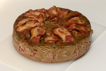 Mouthwatering meat pie topped with crispy bacon slices, showcasing a blend of flavors on a simple surface.の写真素材