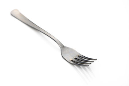 Sleek fork showcases its elegant curves and reflections on an immaculate white surface, indicating its dining use.の写真素材