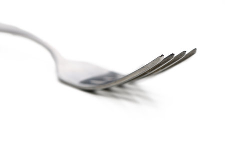A polished metal fork is centered on a smooth white surface, highlighting its sleek lines and simplicity in design.の写真素材