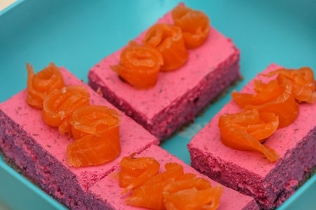 Colorful dessert squares showcase a smooth pink layer topped with sweet orange curls, enticing everyone.の写真素材