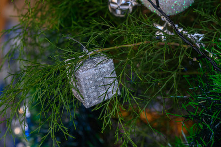 A shimmering silver cube ornament dangles among lush green branches, capturing the magic of the holiday spirit.の写真素材