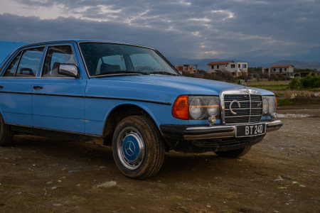 A vintage blue sedan stands proudly near rustic houses as the sun sets, illuminating a colorful sky.の写真素材