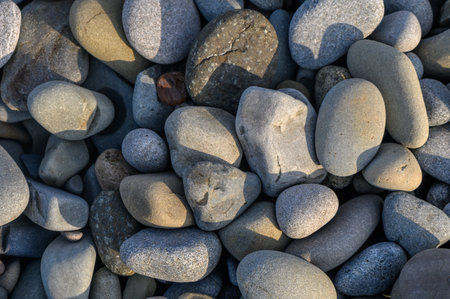 Smooth, round pebbles of various sizes rest together on a serene riverbed, glistening in soft...