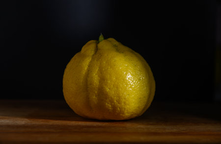 A beautifully shaped yellow lemon sits on a wooden table, illuminated gently to accentuate its...