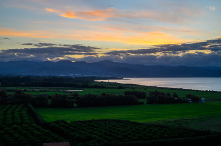 Golden sunset hues light up serene fields, with majestic mountains in the distance reflecting...