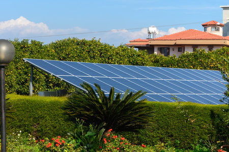 Solar panels gleam under the bright sun, surrounded by lush greenery and colorful flowers in a tranquil garden setting.の写真素材