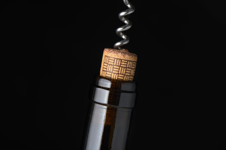 A close-up view shows a corkscrew pulling a cork from a wine bottle, highlighting rich textures and tones.の写真素材