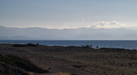Calm waters gently meet the sandy shore as distant mountains fade into a dreamy twilight glow.