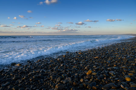 Waves gently crash on a rocky beach while clouds drift across a vibrant sky during the beautiful...