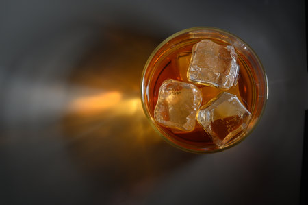 A clear glass filled with a beverage and ice cubes sits on a dark surface, evoking a serene summer vibe.の写真素材