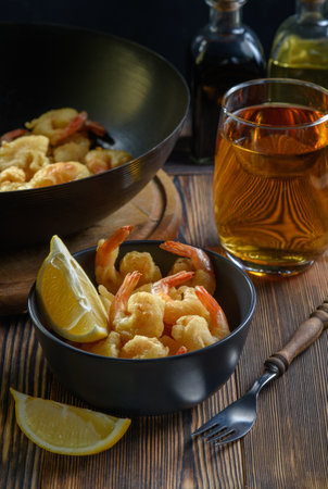 Delightful shrimp served in a black bowl accompanied by fresh lemon and a glass of amber beverage on a wooden tableの写真素材
