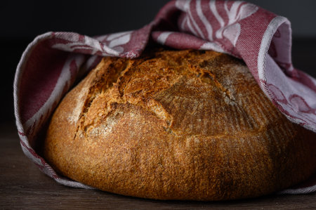 Golden crusted bread awaits to be sliced, wrapped warmly in a cloth, inviting warmth and comfort to the kitchen.の写真素材