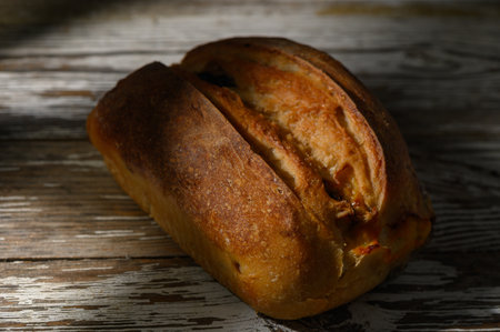 Freshly baked loaf with a golden crust lies on aged wood, basking in the gentle glow of afternoon...