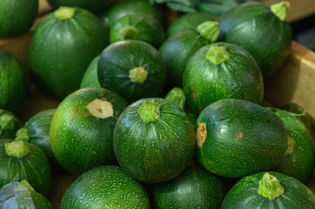 Vibrant zucchinis are stacked artistically, showing their glossy skin and unique round shapes in the market.の写真素材