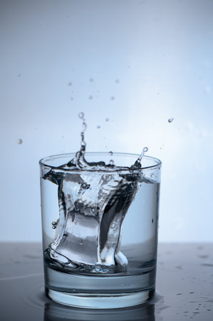 Sparkling drop leaplets from the glass as an ice cube makes a dramatic splash in clear water, creating a refreshing and dynamic scene that captures the elegance of simplicity.の写真素材
