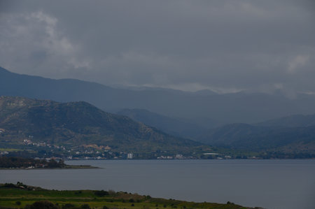 A peaceful lakeside village lies at the foot of majestic mountains, shrouded in a blanket of gray...