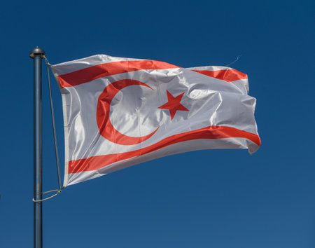 The vibrant flag of Northern Cyprus flutters against a clear blue sky, showcasing a striking design of a red crescent moon and star on a white background, representing cultural pride and unity.の写真素材