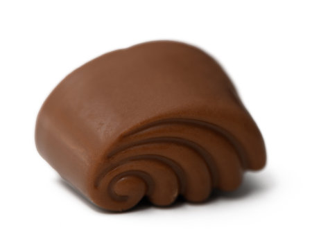 A beautifully crafted piece of chocolate resembling a wave rests gracefully on a soft white surface. Its rich color and intricate design beckon chocolate aficionados for a delightful treat.の写真素材