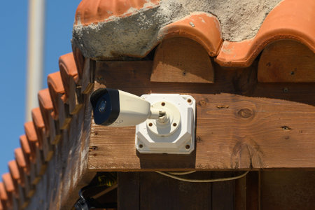 A surveillance camera is installed on a wooden structure with a terracotta roof, looking out to the...