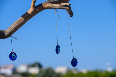 Three vibrant blue protective charms dangle from a weathered branch against a brilliant azure backdrop. This serene coastal setting invites tranquility and peace.の写真素材
