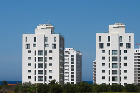Two contemporary white residential buildings stand tall along the coastline, reflecting sunlight. Surrounding greenery enhances the serene atmosphere, making it an inviting urban retreat by the sea.の写真素材