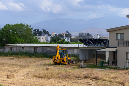 A bright yellow tractor parked near a traditional village house in Cyprus, with stunning mountains...