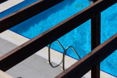 Top-down view of a metal ladder in a swimming pool with clear blue water. Geometric composition with sunlight reflections and summer vibes.の写真素材